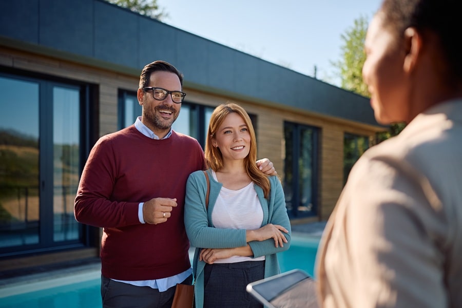 Couple meeting a real estate agent outside a modern house by a pool, smiling and chatting