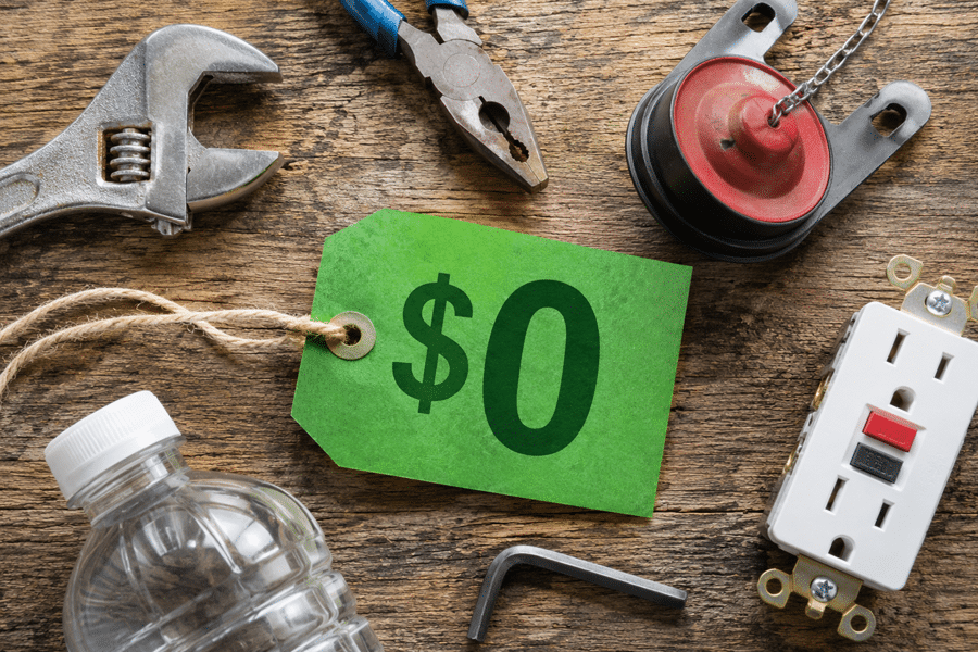 Green price tag reading $0 among repair tools on a wooden workbench (wrench, pliers, pulley, outlet).